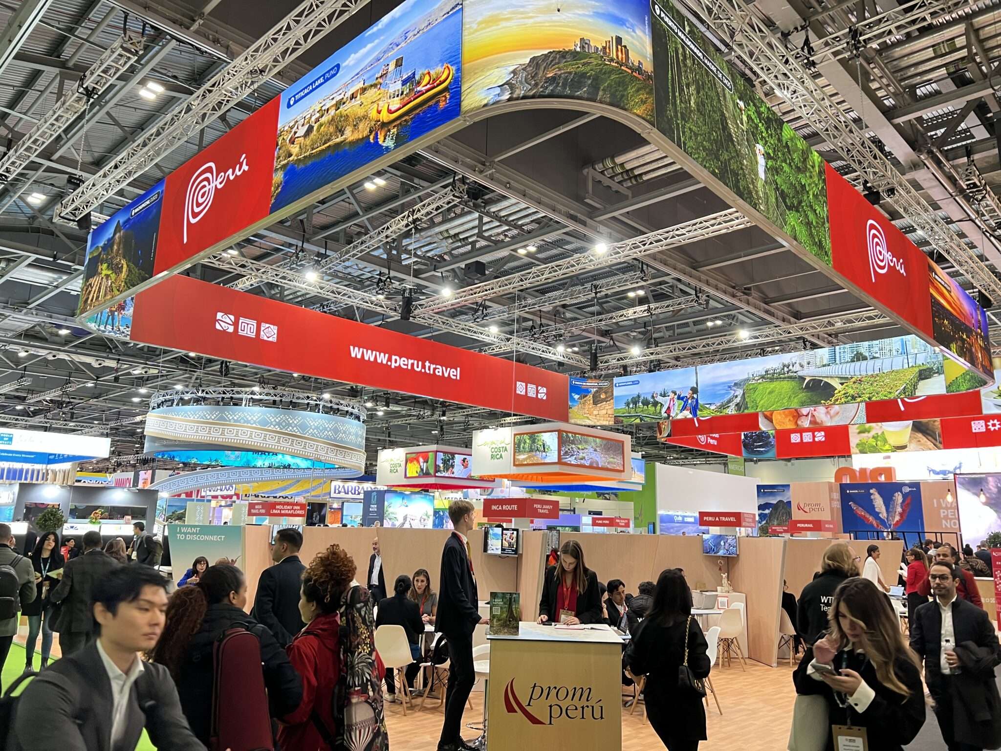 Large modular exhibition booth with red overhead hanging t3 lightbox banners and world travel branding built using T3 Systems display structures.