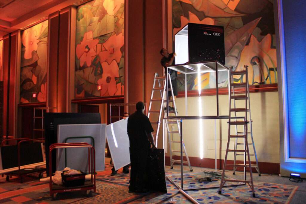 Technicians installing a modular illuminated T3 exhibition lightbox frame during stand setup.