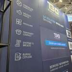 Custom exhibition stand with angled panels, integrated lighting, and service messaging at C!Print Lyon
